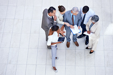 Image showing Paperwork, tablet and business people in meeting in lobby of office in collaboration. Documents, digital technology and high angle of professional financial advisors in discussion for teamwork.