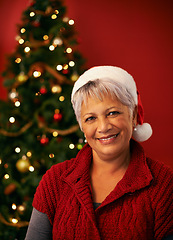 Image showing Christmas, smile and portrait of senior woman in studio for holiday celebration by tree isolated on a red background. Xmas, mature and face of happy female person in hat for festive party in Brazil