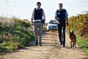 Image showing Detective, dog and walk in field for robbery or crime scene with car for search, safety and law enforcement. Policeman, investigation and uniform in outdoor working at countryside with gravel road