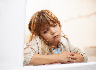 Image showing Window, sitting and child in house for bored, lonely or disappointed for rain or weather outdoor. Young girl or kid and sadness or sick in home for cold season and wait for play for childhood