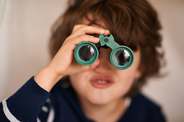 Image showing Boy, kid and binocular with toys and playing, closeup of fun and innocent with search or surveillance. Investigate, looking or curiosity with discovery on adventure, playful with games and activity