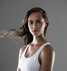 Image showing Woman, serious in portrait and confidence for fitness, strong and determined with sweat from workout on grey background. Hair in wind, athlete for sports and exercise with pride and power in studio