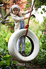 Image showing Portrait, young girl and swing in garden, nature and entertainment in playground. Child, freedom and tyre for childhood development in forest, woods or park on weekend or holiday in autumn season