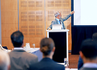 Image showing Senior, businessman and presentation with laptop on projector for meeting, staff training or seminar at conference. Man, CEO or speaker talking on podium to group for corporate showcase at workshop