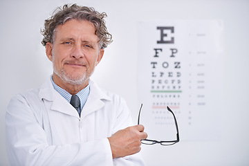 Image showing Eye, test and portrait of optometrist in clinic with glasses to check vision and exam in healthcare. Mature, doctor and reading letters on wall in medical assessment for contact lenses or eyesight