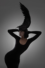 Image showing Bird, fashion and art style woman in a studio with head piece, feather hat and abstract with unique creativity. Crow, silhouette and shadow with fantasy and with goth clothes and grey background