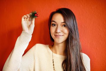 Image showing Christmas, portrait and happy woman with holly branch in hand and winter celebration by red background. Young, person and smile on face with holiday decoration, gift and symbol of peace or goodwill