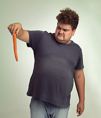 Image showing Plus size, diet and disgusted man with carrot for health, nutrition and wellness in studio by white background. Weight loss, vegetable and unhappy male person for detox, wellbeing and vegan food