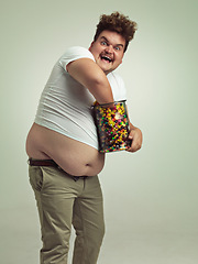 Image showing Sweets, crazy and portrait of man in studio for luxury snacks, sugar and dessert in jar. Comic, funny facial expression and plus size person with glass container for unhealthy diet on background