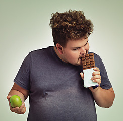 Image showing Man, apple and chocolate in studio with choice of junk food, sweet or diet for wellness. Plus size, male person eating and decision, fruit or candy for nutrition, lose weight and healthy lifestyle