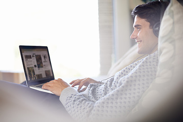 Image showing Laptop, headphones and happy man in home typing, relax or listening to sound of radio podcast on sofa. Computer, music and smile of person in lounge for internet, social media and streaming audio