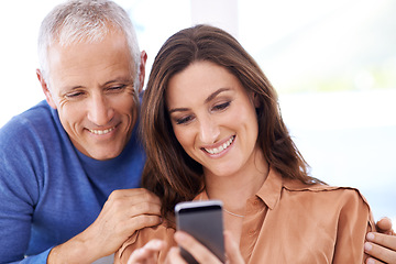 Image showing Couple, smartphone and smile in home to relax with reading, search and mobile app for contact with bonding. People, woman and mature man with phone for notification, typing or web connection in house