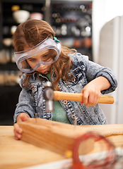 Image showing Chilld, construction and hammer a nail in workshop, play and game in kitchen of home. Female person, girl and safety glasses or tool for wood project or hobby, carpentry and remodeling or manufacture