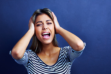 Image showing Woman, noise and cover ears in studio with stress, mental health and shouting with anxiety by blue background. Girl, person and model with tinnitus, frustrated and stop sound with hands on head