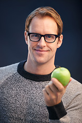 Image showing Man, apple and glasses in studio portrait with smile for choice, diet or health by dark background. Person, model and happy with green fruit with pride for decision, vegan nutrition or organic snack