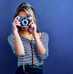 Image showing Woman, photographer and camera by face in studio for creativity, media and journalist job by blue background. Girl, retro lens and photography with photoshoot for magazine, collection and newspaper