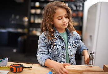 Image showing Girl, carpentry and hammer a nail in workshop, play and game in kitchen of home. Female person, child and equipment or tool for wood project or hobby, construction and remodeling or manufacture