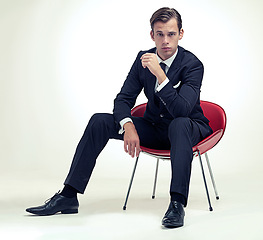 Image showing Portrait, man and vintage suit on chair in studio and serious in formal fashion by white background. Young model, face or confidence in elegant clothes for event, relax or smoking in tuxedo by party