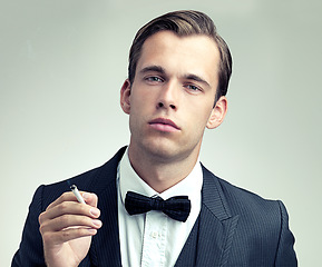 Image showing Portrait, suit or young gentleman smoking a cigarette in studio, confidence or vintage fashion by white background. Face, serious and man in retro clothes or tuxedo, bow tie and class at formal event
