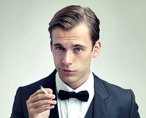 Image showing Portrait, elegant or young man smoking a cigarette in studio, formal or vintage fashion by white background. Face, attitude or gentleman in retro suit or tuxedo, bow tie or habit of tobacco at event