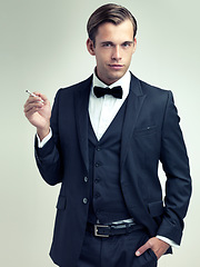 Image showing Portrait, elegant or young gentleman smoking a cigarette in studio, confidence or vintage fashion by white background. Face, serious and man in retro suit or tuxedo, bow tie and class at formal event