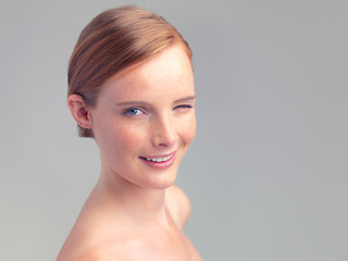 Image showing Portrait, wink and skincare of happy woman for beauty, shine or mockup space in studio isolated on a gray background. Face, smile and ginger model with cosmetics, makeup or treatment for dermatology