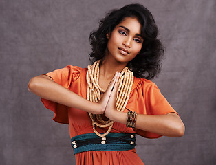 Image showing Indian woman, fashion and smile with jewelry in studio on grey background with hands together and dress. Portrait, female person and outfit with confidence in traditional necklace and creative look