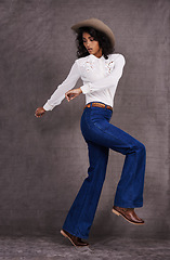 Image showing Woman, fashion and western clothes in studio, wild west and country style on Indian model. Jumping, confident strong female person with trendy hat accessory, culture and isolated on backdrop