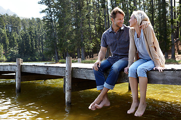 Image showing Couple, lake and sitting on jetty, outdoor and happy for hug on vacation, relax or nature in summer. Man, woman and embrace with smile, care or bonding with connection for love on holiday in Colorado