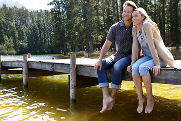 Image showing Couple, lake and sitting on pier, outdoor and happy for hug on vacation, relax or memory in summer. Man, woman and embrace with smile, care or bonding with connection for love on holiday in Colorado