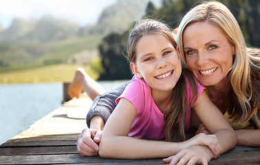 Image showing Mom, daughter and relax on pier by a lake, bonding in nature or camping with holiday, travel and family time. Love, support and trust, woman and young girl outdoor for adventure and fresh air