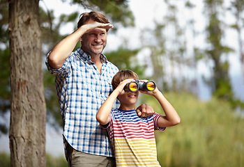 Image showing Father, son and binoculars in nature for outdoor adventure, birdwatching and learning by trees with smile. Dad, child and support for vision, view and search for connection, care or bonding in forest