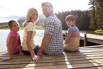 Image showing Parents, lake and children on pier for portrait, happy and sitting on vacation with love in summer sunshine. Mom, dad and kids with smile, care or bonding with family by river on holiday in Colorado