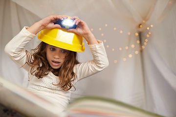 Image showing Girl, child and book for reading with lamp, below and learning with thinking for education in family home. Kid, story and study with light on helmet, language or literacy skills with blanket in house