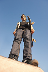 Image showing Skatepark, serious and portrait of man with skateboard practicing for competition with skills. Fitness, hobby and bottom view of young male skater on ramp for outdoor training with blue sky.