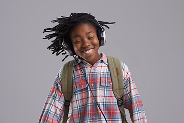 Image showing Black man, music and smile of a teenager with hip hop and rap audio in a studio. Relax, backpack and student with headphones streaming a radio song before school with a happy kid and grey background