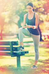 Image showing Woman, exercise and listening to music in park, fitness and commitment or training for healthy body. Young lady, smartphone and runner with streaming audio, technology and morning workout in nature