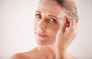 Image showing Eyebrows, tweezer and portrait of model on a white background for facial grooming or hair removal. Beauty, salon and face of mature female person isolated in studio plucking or tweezing for skincare