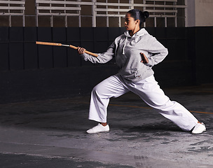 Image showing Martial arts, woman and fitness with weapon for training with nunchaku, exercise and practice for self defence at night. Karate, athlete and workout for fighting, discipline or technique in warehouse