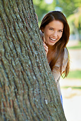 Image showing Woman, park and tree with hide, smile and portrait with happiness and green fun for nature. Lady, laugh and sun with grass, forest and happy for excited playful summer with optimism and sunshine