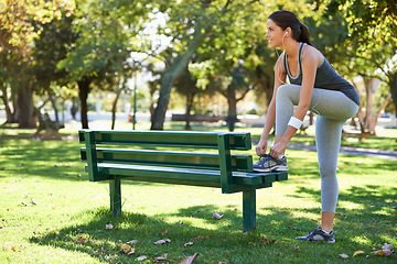 Image showing Happy woman, runner or tying shoelace in outdoor, earphones or streaming audio for exercise in nature. Lady, smile or music for wellness on jog, fitness or training performance in park in montreal