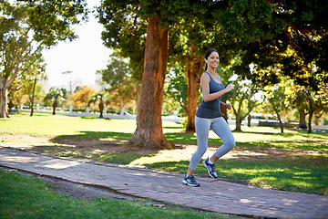 Image showing Happy woman, running and training in portrait in park, music and streaming audio for exercise in nature. Athlete, smile face and wellness with headphones for fitness and runner in outdoor in montreal