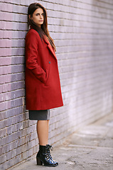 Image showing Winter, fashion and woman on wall with jacket in city and travel with cool style in red coat. Streetwear, clothes and girl outdoor on building background with confidence and pride in New York morning