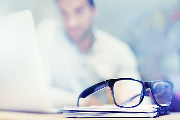 Image showing Blur, notebook and glasses on desk with man in office for planning, schedule and agenda on table. Laptop, eyewear or worker copywriting with diary journal for business, administration or email on web