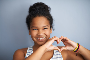 Image showing Girl, portrait and heart shape with hands in studio for love, happiness and happy by grey background. Female, child and smile face with care sign for charity, donation and symbol to support or health