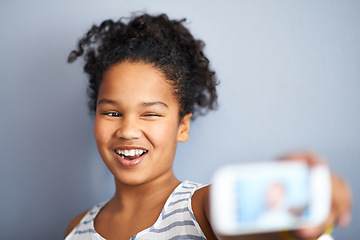 Image showing Young girl, selfie and wink in studio for happiness, closeup and vibrant teen by grey background. Child, smile and excited teenager with profile picture, technology and update on social media