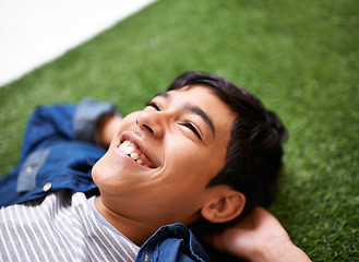 Image showing Boy, relax and lying on grass in backyard, resting and enjoying summer and nature outdoor. Children, smile and sunshine after school in park, adorable kid and joyful in garden or lawn with happiness