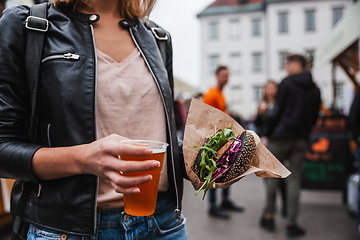 Image showing Close up of woman hands holding delicious organic salmon vegetarian burger and homebrewed IPA beer on open air beer an burger urban street food festival in Ljubljana, Slovenia.