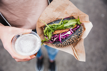 Image showing Close up of woman hands holding delicious organic salmon vegetarian burger and homebrewed IPA beer on open air beer an burger urban street food festival in Ljubljana, Slovenia.