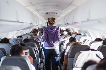 Image showing Interior of airplane with passengers on seats and female traveler walking the aisle. Commercial economy flight service concept.